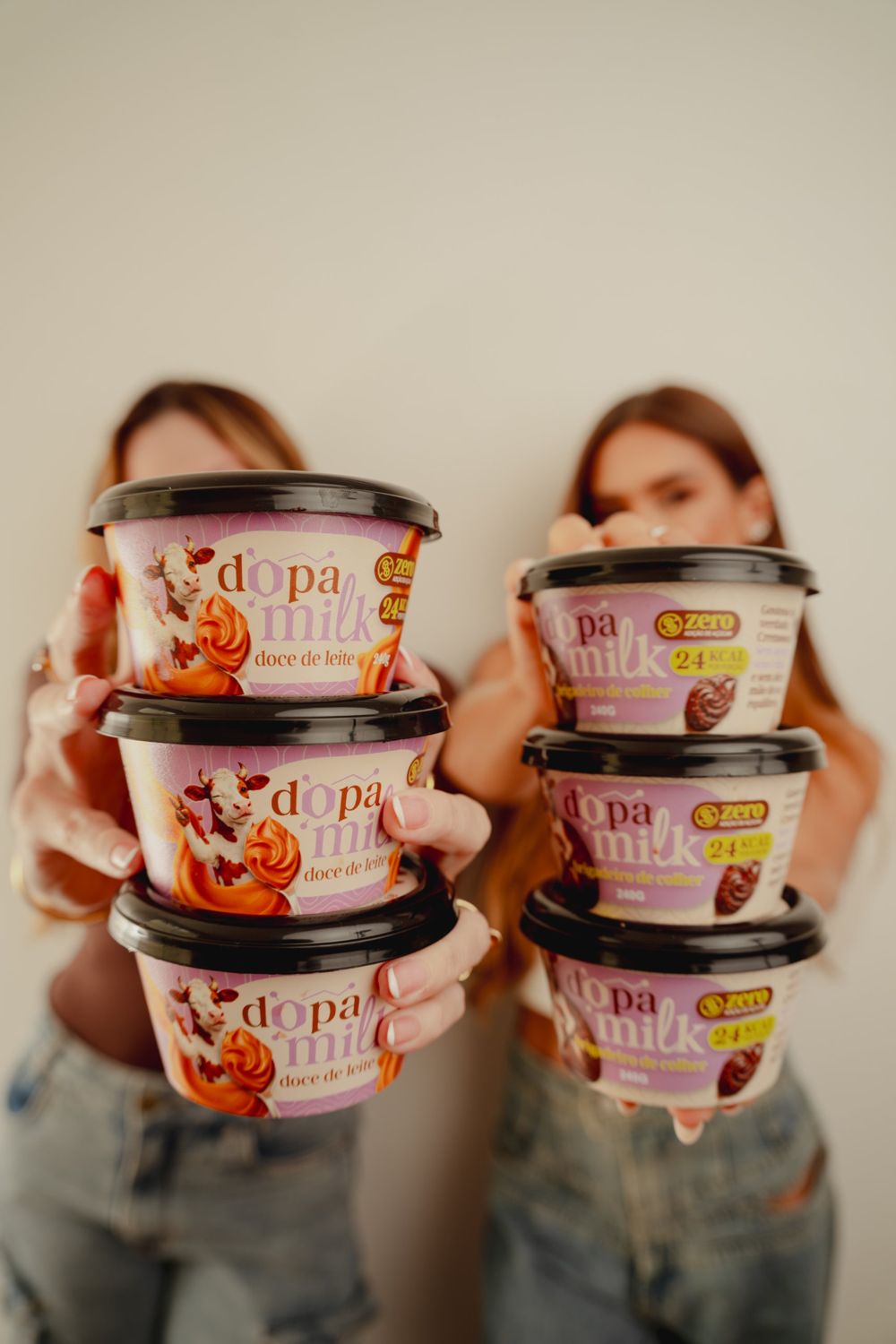 duas mulheres segurando pilhas de potes de doce de leite e brigadeiro Dopa Milk